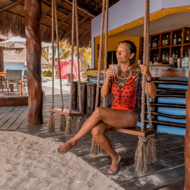 Woman sipping a cocktail on the swing at Playa Norte Beach Club