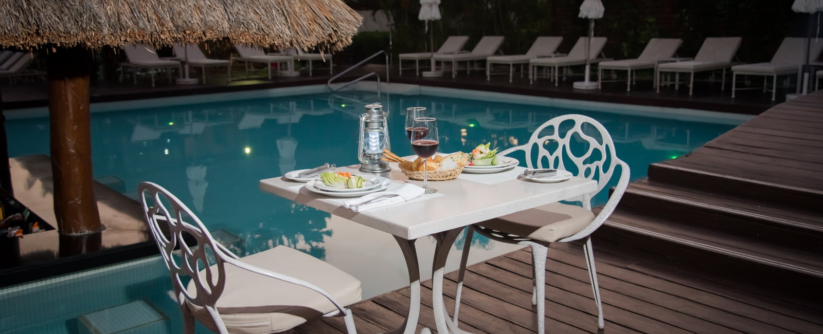 Mesa con servicio, comida y vino para dos en la piscina