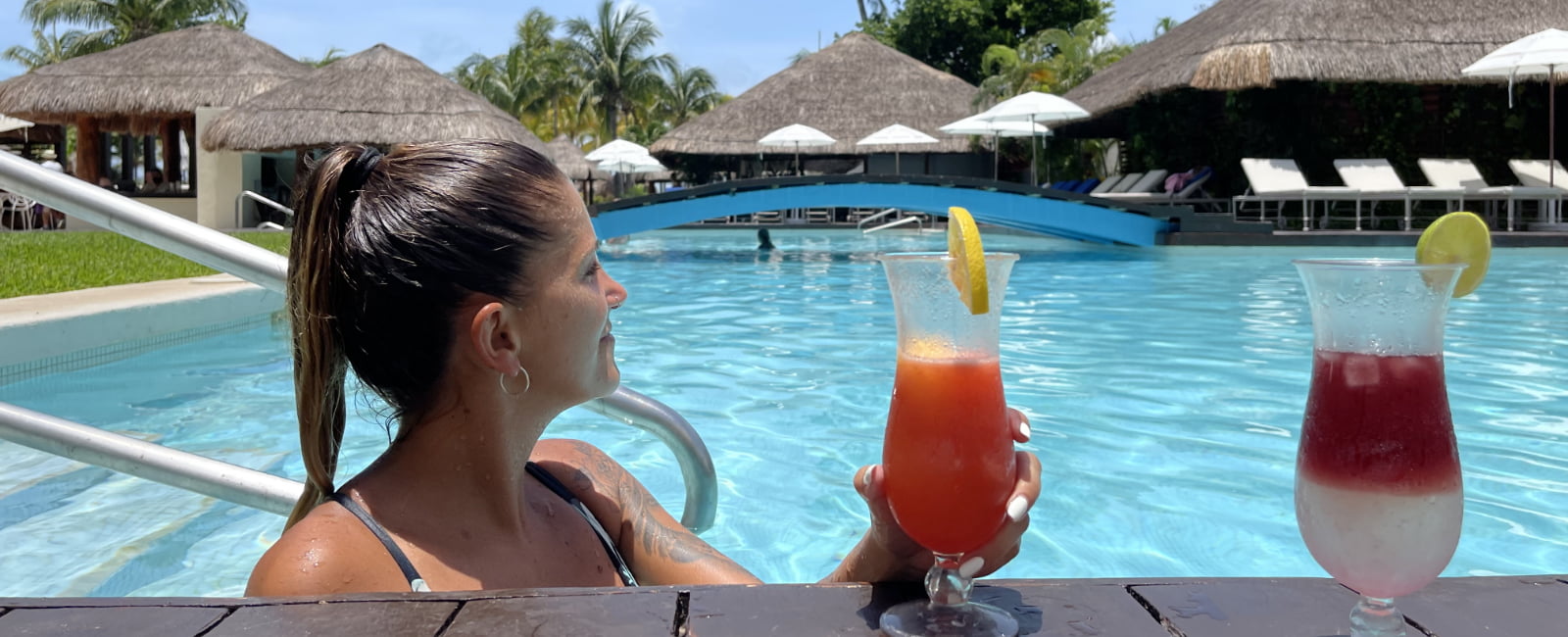 Mujer relajada en las escaleras de la piscina tomando un cocktail